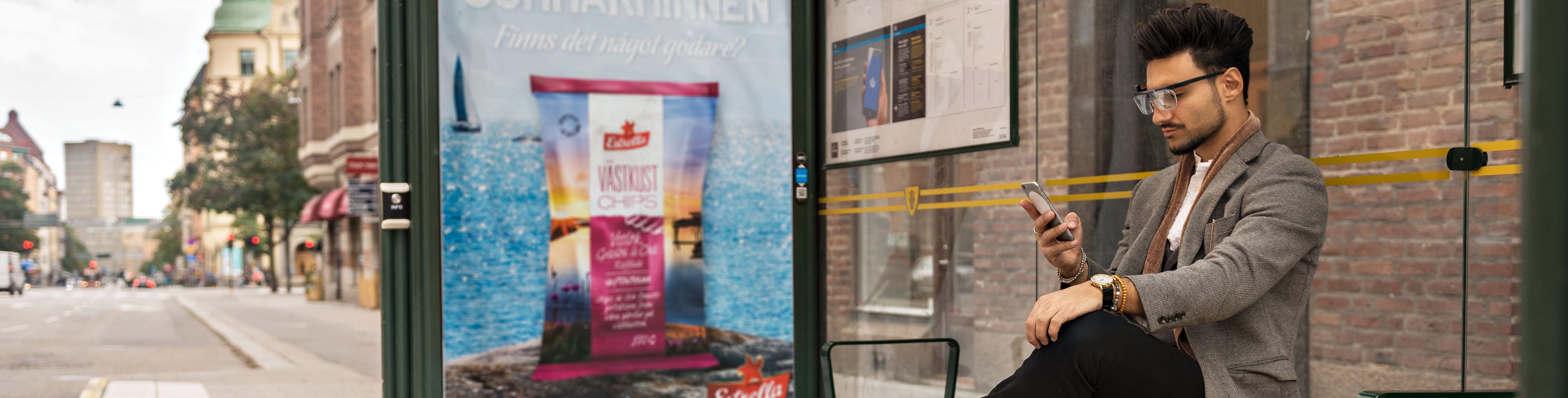 Man at a bus shelter looking at his mobile